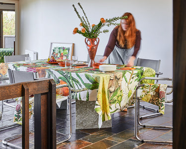 Woman arranging flowers in a modern kitchen with wooden beams and a large window.